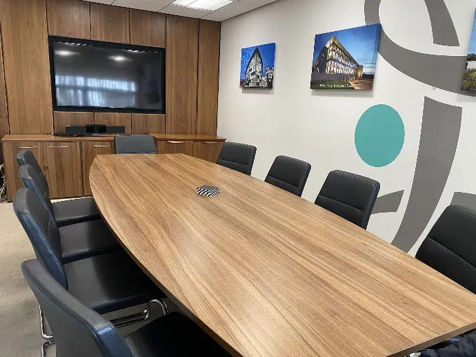 Board room with large oval table surrounded by chairs. Large TV on the wall for comms